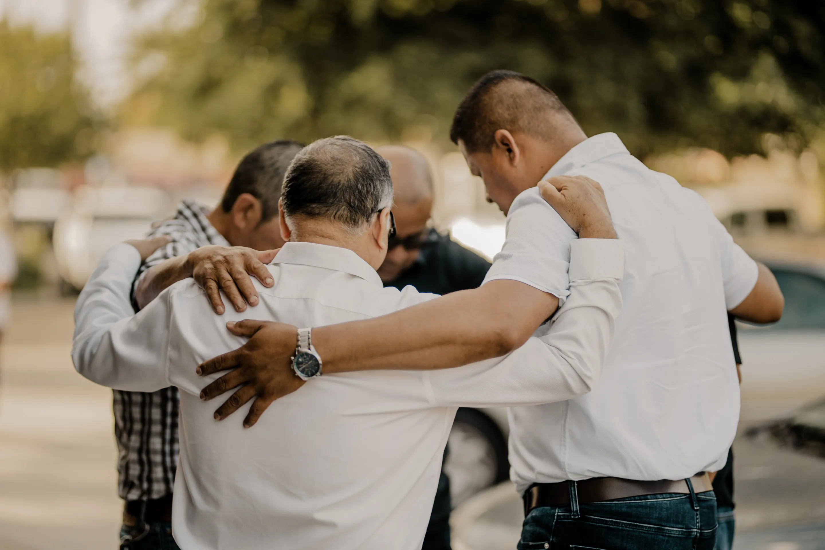 Un grupo de hombres abrazados en oración.